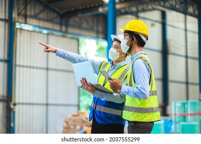 Team Engineers And Foreman Wear A Mask, Hard Hat, And Vest. Standing, Consult Discuss Industrial Production Management Through Data Files With In Mask Factory. Employees Working In The Background.