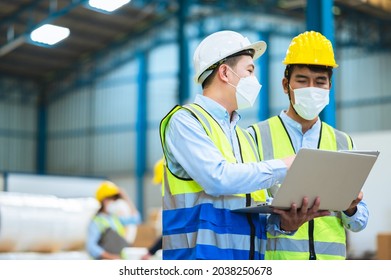 Team Engineers And Foreman Wear A Mask, Hard Hat, And Vest. Standing, Consult Discuss Industrial Production Management Through Data Files With In Mask Factory. Employees Working In The Background.