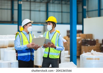 Team Engineers And Foreman Wear A Mask, Hard Hat, And Vest. Standing, Consult Discuss Industrial Production Management Through Data Files With In Mask Factory. Employees Working In The Background.