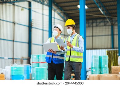 Team Engineers And Foreman Wear A Mask, Hard Hat, And Vest. Standing, Consult Discuss Industrial Production Management Through Data Files With In Mask Factory. Employees Working In The Background.