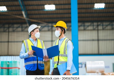 Team Engineers And Foreman Wear A Mask, Hard Hat, And Vest. Standing, Consult Discuss Industrial Production Management Through Data Files With In Mask Factory. Employees Working In The Background.