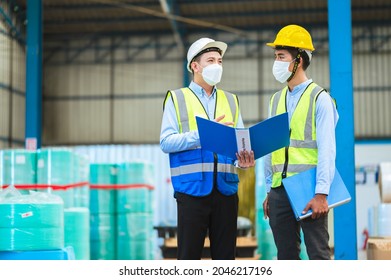 Team Engineers And Foreman Wear A Mask, Hard Hat, And Vest. Standing, Consult Discuss Industrial Production Management Through Data Files With In Mask Factory. Employees Working In The Background.