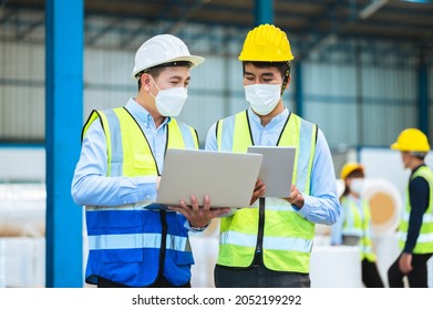 Team Engineers And Foreman Wear A Mask, Hard Hat, And Vest. Standing, Consult Discuss Industrial Production Management Through Data Files With In Mask Factory. Employees Working In The Background.