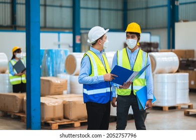 Team Engineers And Foreman Wear A Mask, Hard Hat, And Vest. Standing, Consult Discuss Industrial Production Management Through Data Files With In Mask Factory. Employees Working In The Background.