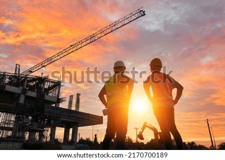 A team of engineers on a construction site pass a blurry construction site at sunset.