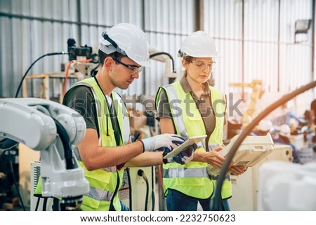 Team of engineers or worker is controlling robot arm machine welding steel, worker using forcing welding with a control screen which is used for precision welding control.