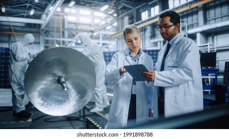 Team Of Engineers Working On Satellite Construction, Use Tablet Computer Talk About Data. Aerospace Spaceship Manufacturing Facility: Team Of Scientists Building Spacecraft For Space Exploration