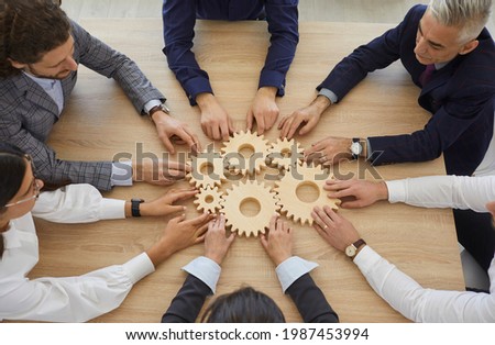 Team of entrepreneurs collaborate and develop effective business system. Group of senior and young business people join gearwheels as metaphor for good cooperation and teamwork, high angle, from above