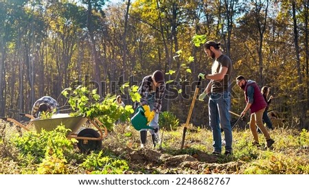 Team of environmental activists planting trees in garden at forest and taking care of nature. Outdoor. Caucasian men and women working in park with tree seedlings on sunny day.