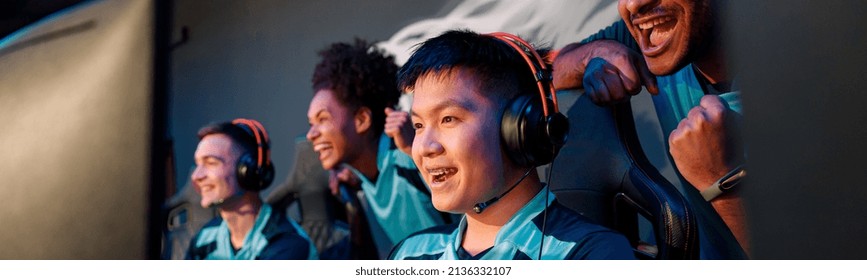 Team of excited cybersports gamers looking at PC screen and celebrating success while participating in esports tournament in gaming club