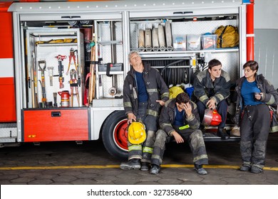 Team Of Exhausted Male And Female Firefighters At Truck In Fire Station