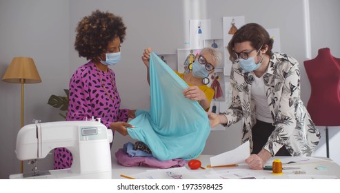 Team of fashion designer wearing safety mask discussing sketch and choosing fabric in workshop. Diverse stylist in protective mask developing new cloths collection in studio - Powered by Shutterstock