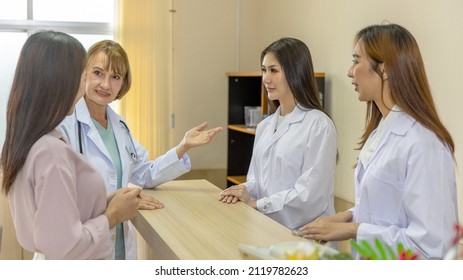 Team Of Female Doctor And Therapists Discuss With Young Outpatient To Diagnose Any Sickness Symptom For Potential Treatment At Clinic Reception Counter