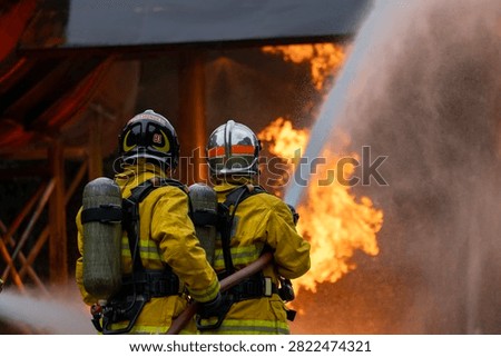 Team of firefighter in fireproof clothes using fog watering hose to put out burning crashing plane with high flame for fire extinguish risk rescue mission and accident