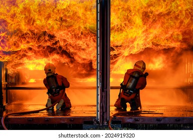 Team Of Firefighters Wearing Full Safety Uniform With Oxygen Tank On The Back Holding Extinguisher Spread Water From Hose And Face To Wide Huge Danger Hot Fire With Brave In Disaster Area.