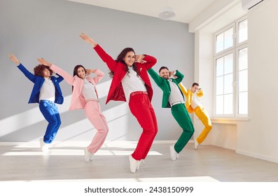 Team of five male and female dancers rehearsing in modern white dance studio. Group of happy, smiling, young people wearing colorful suits doing synchronized tip toe stand movement all together - Powered by Shutterstock