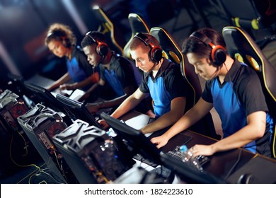 Team of focused professional cybersport gamers wearing headphones playing online video games while sitting in gaming club or in internet cafe