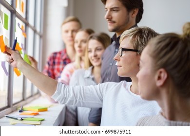 A team of focused work colleagues discussing ideas and brain storming with sticky notes on an office window. - Powered by Shutterstock