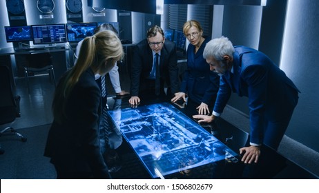 Team of Government Intelligence / FBI Agents Standing Around Digital Touch Screen Table and Tracking Suspect Vehicle Using Satellite Surveillance in the Monitoring Room.