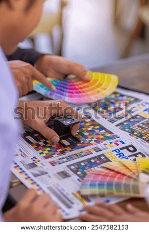 Team graphic designer checking print quality of media graphics proof print and color guides in printing industry. Selected focus