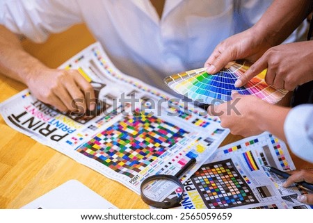 Team graphic designer checking print quality of media graphics proof print and color guides in printing industry. Selected focus