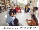 Team of happy business people discussing funny positive stuff in group meeting. High angle shot of diverse corporate company employees and coworkers sitting together around office table and talking