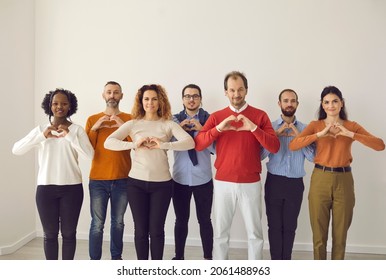 Team of happy multiracial youth and old citizens sending you love, support and gratitude. Studio group portrait of thankful young and mature people standing together and doing heart shape hand gesture