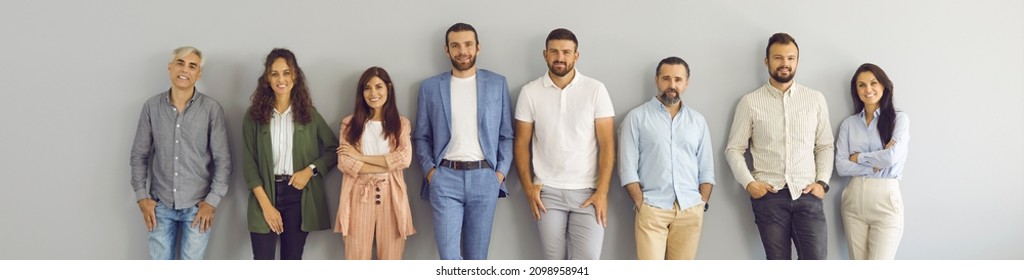 Team Of Happy Smiling Business People Standing Against Grey Studio Background. Banner With Group Portrait Of Confident Successful Senior And Young Men And Women In Smart And Casual Clothes