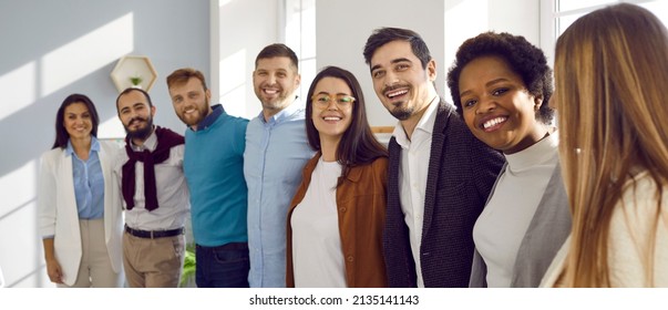 Team Of Happy United Young Business People Hugging Each Other. Diverse Mixed Race Group Of Men And Women Standing In Row In Their Office, Huddling And Smiling All Together. Unity And Teamwork Concept