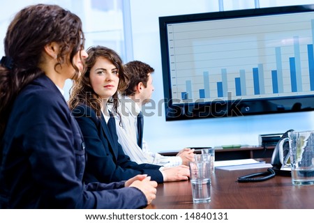 Team of happy young businesspeople having meeting in boardroom at office in front of a huge plasma TV screen, indoor, smiling.