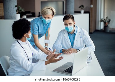 Team of healthcare workers cooperating while using laptop on a meeting at medical clinic. They are wearing face masks due to coronavirus pandemic.  - Shutterstock ID 1865708293