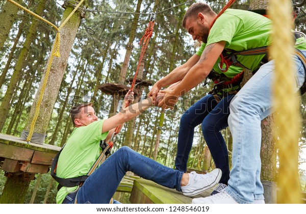 Team helps man climb the high ropes course during a\
team building event