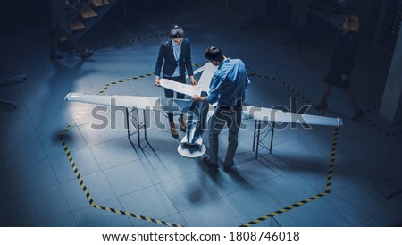 Team of Industrial Aerospace Engineers Work On Unmanned Aerial Vehicle Concept. Designers Work on Pilotless Drone. Industrial Facility with Aircraft Capable of Surveillance and Military. Elevated Shot