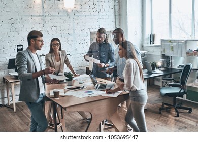 Team of innovators. Group of young modern people in smart casual wear discussing business while standing behind the glass wall in the creative office - Shutterstock ID 1053695447
