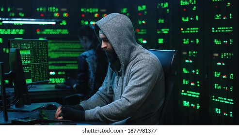 Team of internationally wanted hackers using computer for organizing massive data breach attack. Secret location surrounded by displays and servers. - Shutterstock ID 1877981377