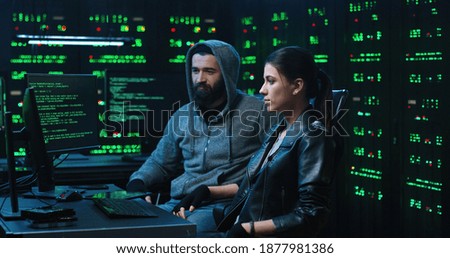 Team of internationally wanted hackers using computer for organizing massive data breach attack. Secret location surrounded by displays and servers.