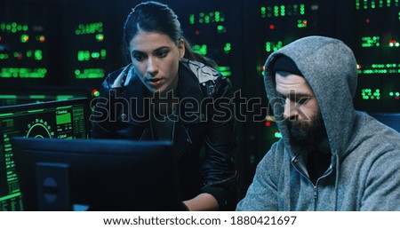 Team of internationally wanted hackers using computer for organizing massive data breach attack. Secret location surrounded by displays and servers.