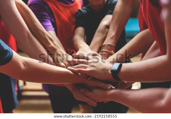 Team of kids children basketball players stacking\
hands in the court, sports team together holding hands getting\
ready for the game, playing indoor basketball, team talk with\
coach, close up of hands