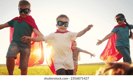 team of kids superheroes run. happy family kid concept. a group of children playing superheroes in capes and masks run through the grass at sunset. success business striving dream for goal concept