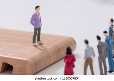 Team leader addressing a group of miniature figures of business colleagues standing on an elevated wooden board, as the men and women gather below to listen - Shutterstock ID 1630009804