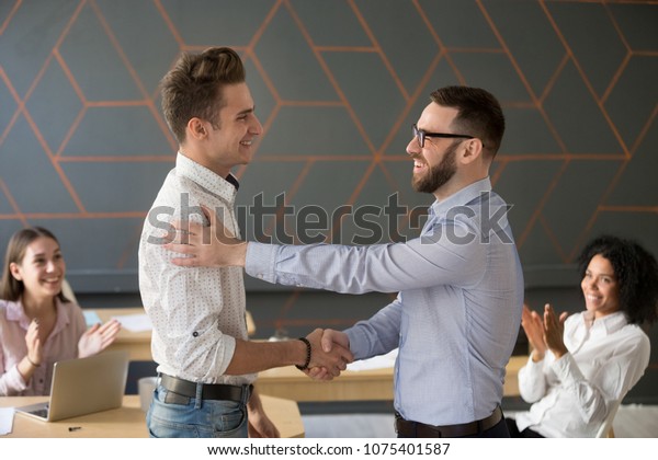 Team leader handshaking employee congratulating\
with professional achievement or career promotion, thanking for\
good project result while team supporting applauding, appreciation\
recognition concept