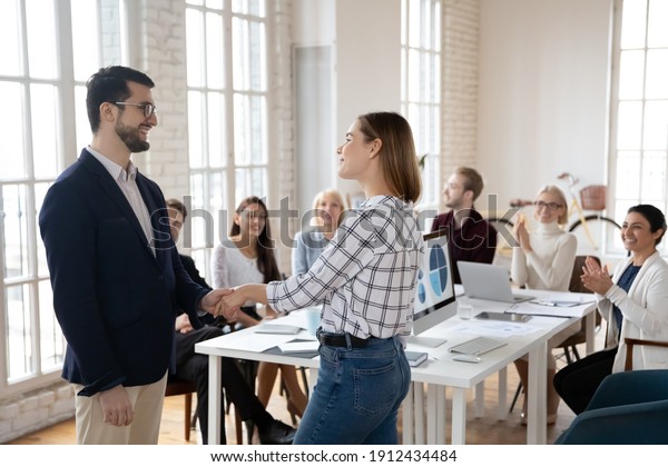 Team leader thanking best employee for work
achievements. CEO and manager shaking hands. Staff welcoming and
applauding new hired employee in conference room. Recognition,
acknowledgement concept