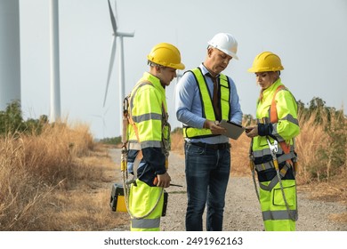 Team of maintenance engineers using tablets working on a wind farm and discussing clean energy production. The concept of alternative renewable energy for future