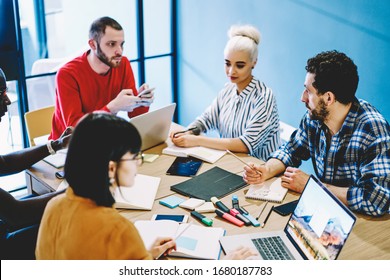 Team of male and female multiracial designers sitting at table together during working brainstorming session using gadgets for analyzing and research, group of smart young 20s students prepare project