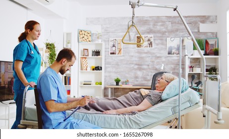 Team Of Male And Female Nurses Checking An Old Lady Lying In Hospital Bed In A Retirement Home