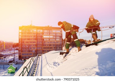 Team of male workers clean roof of building from snow with shovels in securing belts of mantra. - Shutterstock ID 790371025