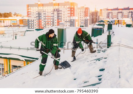Team of male workers clean roof of building from snow with shovels in securing belts of mantra.