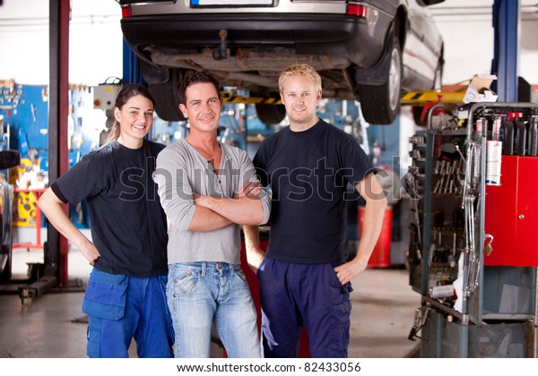 A team\
of mechanics in a shop with a car on a\
hoist