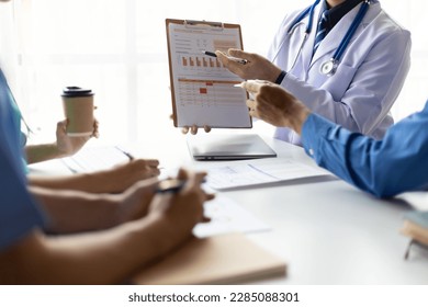 Team, medical analysts and doctors consulting with paperwork of graphs, data and charts in hospital conference room. Healthcare staff discussing statistics, results of research and innovation. - Powered by Shutterstock