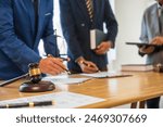 A team meeting of business people and a lawyer in formal suits is taking place at a desk, discussing a contract and various aspects of the law and litigation.